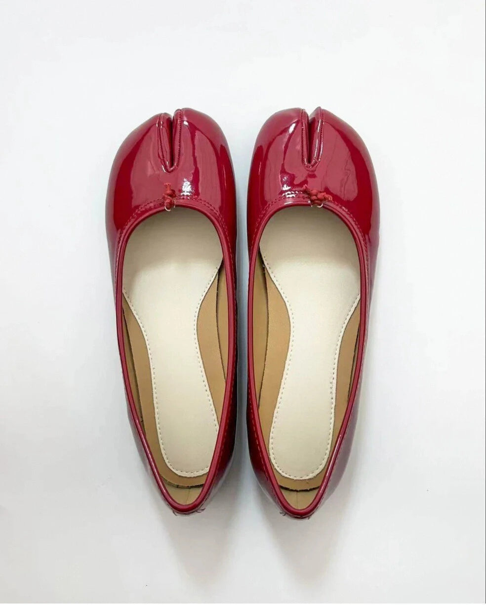 A pair of red patent leather Tabi ballet flats placed side by side on a white surface.