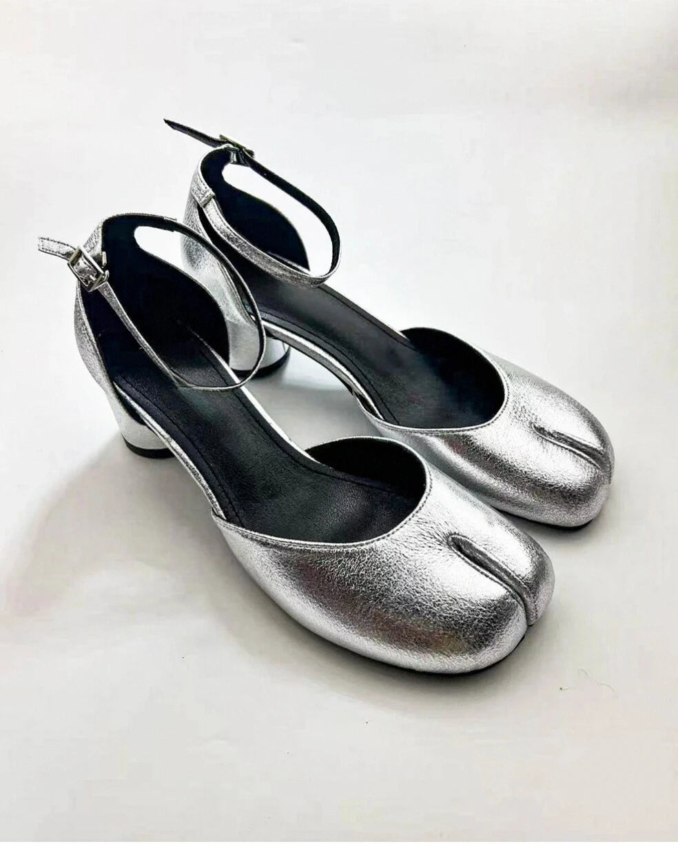 A pair of silver Tabi ankle strap sandal pumps with a low heel and microfiber leather upper and lining.