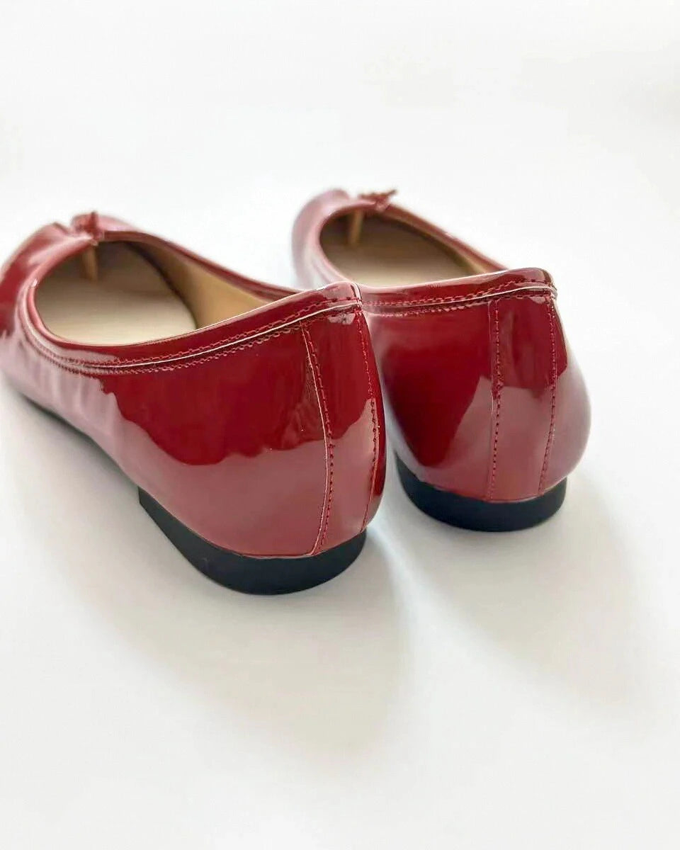 A pair of red patent leather ballet flats with bow detail on the instep.